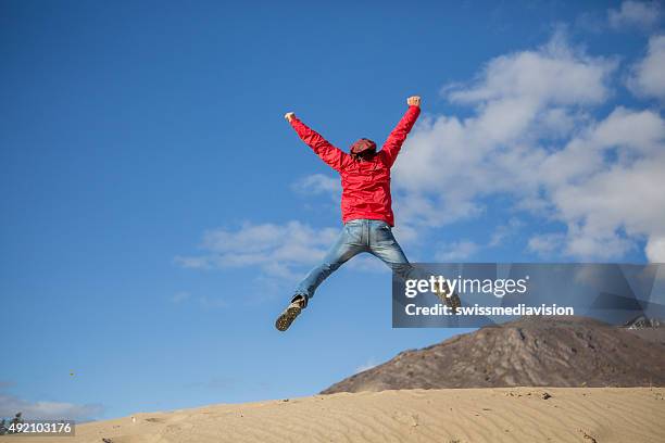 young cheerful man in desert jumping makes cross shape - xes 個照片及圖片檔