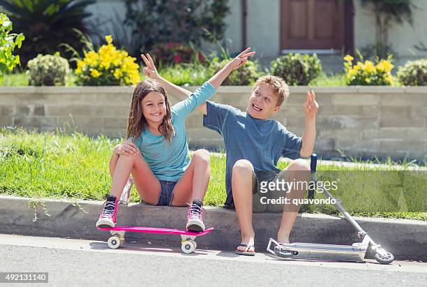 jungen und mädchen flirten auf gehweg mit skateboard und scooter - roller skates stock-fotos und bilder