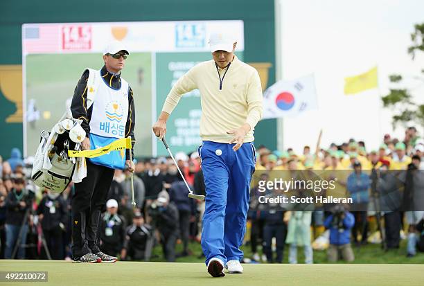 Sang-Moon Bae of the International Team picks up his ball on the 18h green in his match against Bill Haas of the United States Team as his caddie...
