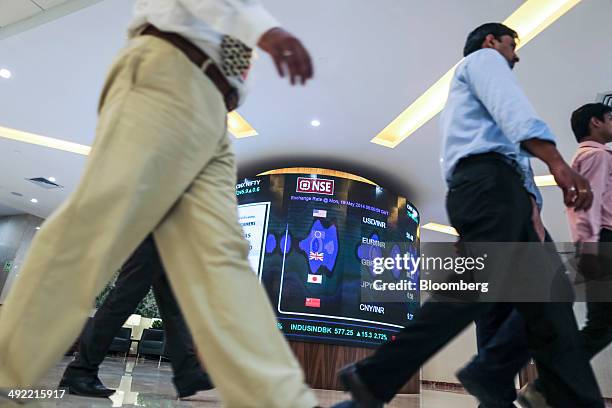 Employees walk past an electronic board displaying the rupee's exchange rates against the U.S. Dollar, from top, euro, pound sterling, Japanese yen...