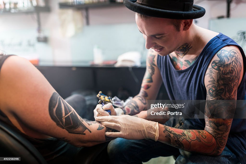 Artista de hacer el tatuaje en la mano de hombre cliente en estudio