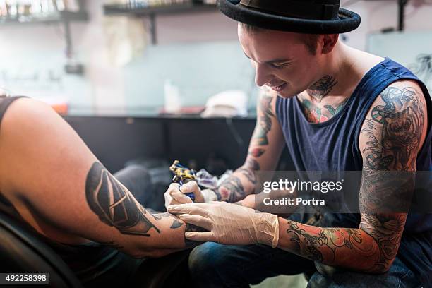 artist making tattoo on male customer's hand in studio - tatoeage stockfoto's en -beelden