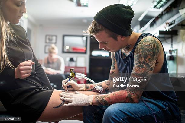 expert tattooing female customer's lap - tatoeage stockfoto's en -beelden