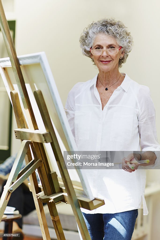 Confident senior woman standing by canvas at porch