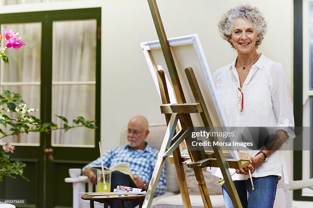 Senior woman standing by canvas at porch