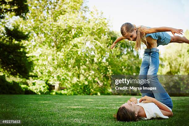 mother lifting daughter with legs in park - junge barfuß stock-fotos und bilder