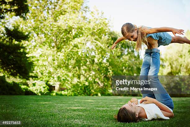mother lifting daughter with legs in park - lying down stockfoto's en -beelden