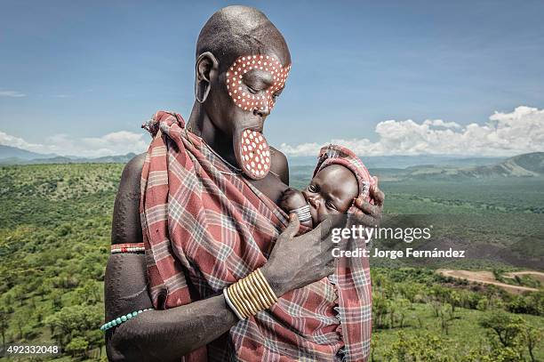 Mursi woman with a lip plate holding her child on a lookout of the Omo valley.
