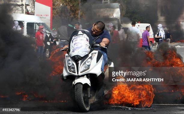 Palestinian man rides his motorcycle past burning tires as protestors clash with Israeli security forces at the Hawara checkpoint, south of the West...