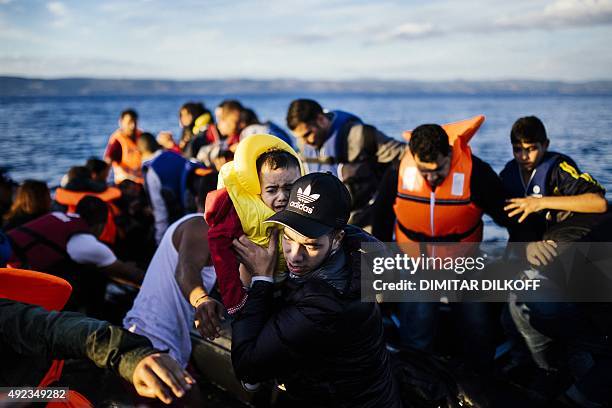 Man carries a child off a rubber dinghy after arriving with other refugees and migrants on the Greek island of Lesbos after crossing the Aegean sea...