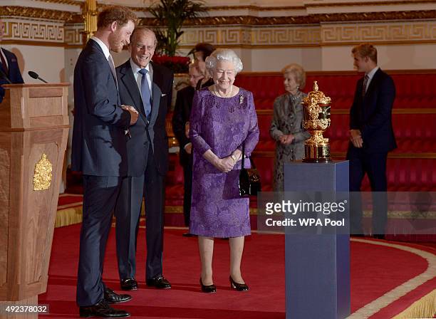 Prince Harry, Prince Philip, Duke of Edinburgh and Queen Elizabeth II look at the Webb Ellis Cup on a plinth during a Rugby World Cup reception at...
