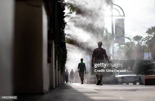 Pedestrians walk under cooling misters in downtown Palm Springs where the temperatures reached the high 90's on October 12, 2015 in Palm Springs,...