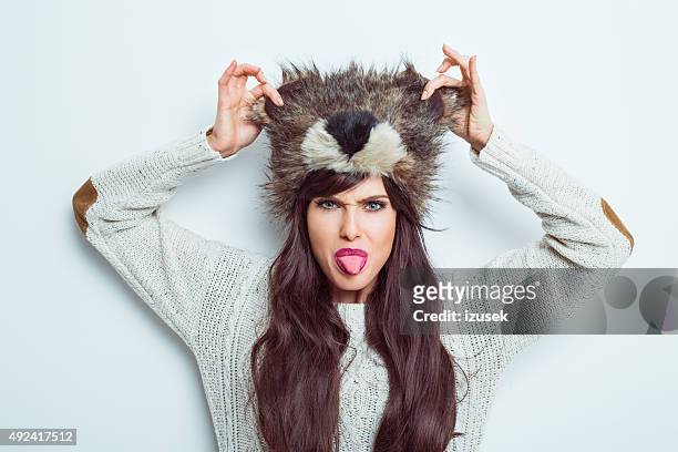 carefree woman wearing fur cap and sticking out her tongue - irony stockfoto's en -beelden