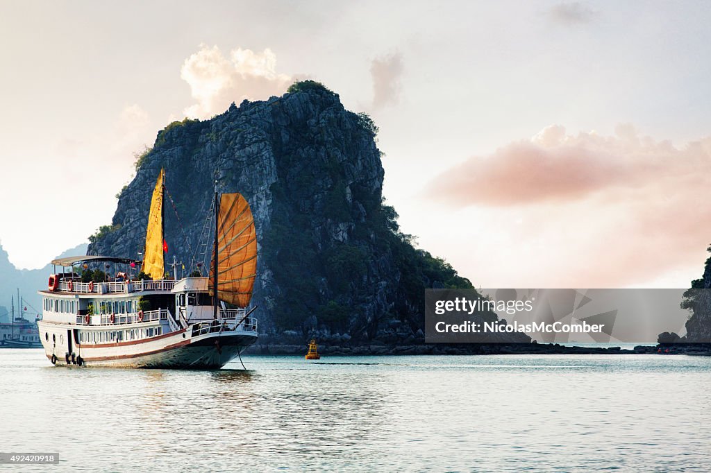 Halong bay Vietnam tourist ship with cliff island at sunset