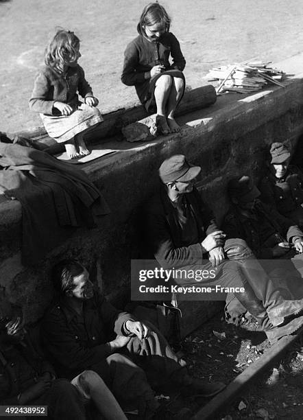 Deux jeunes allemandes observant les prisonniers allemands se reposant sur des rails de chemin de fer en attendant d'etre transferes par les forces...