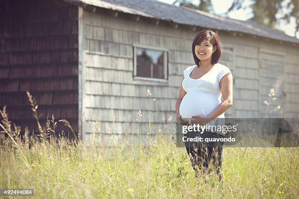 young pregnant teen mom standing by shed - tienerzwangerschap stockfoto's en -beelden