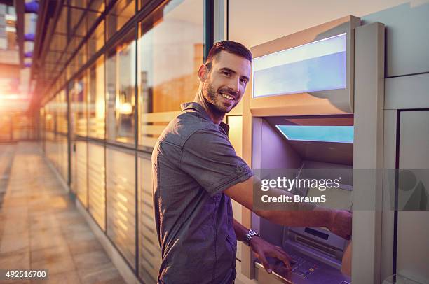 homme d'affaires jeune souriant retirer de l'argent à un distributeur automatique de billets. - dab photos et images de collection