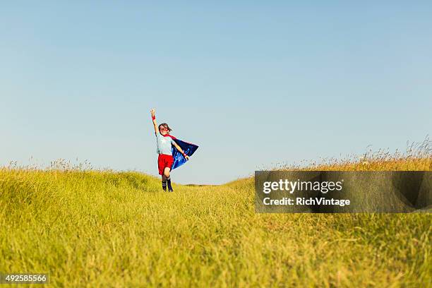 young girl dressed as superhero running in grass - superhero girl stock pictures, royalty-free photos & images