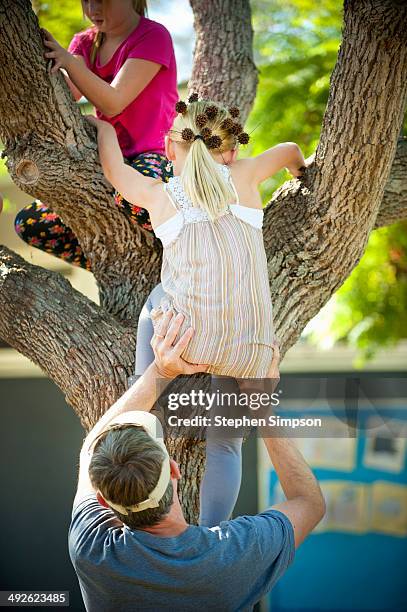 dad helping girls climb a tree - girl bums stock-fotos und bilder