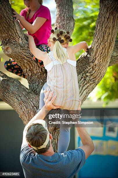 dad helping girls climb a tree - girl bums 個照片及圖片檔
