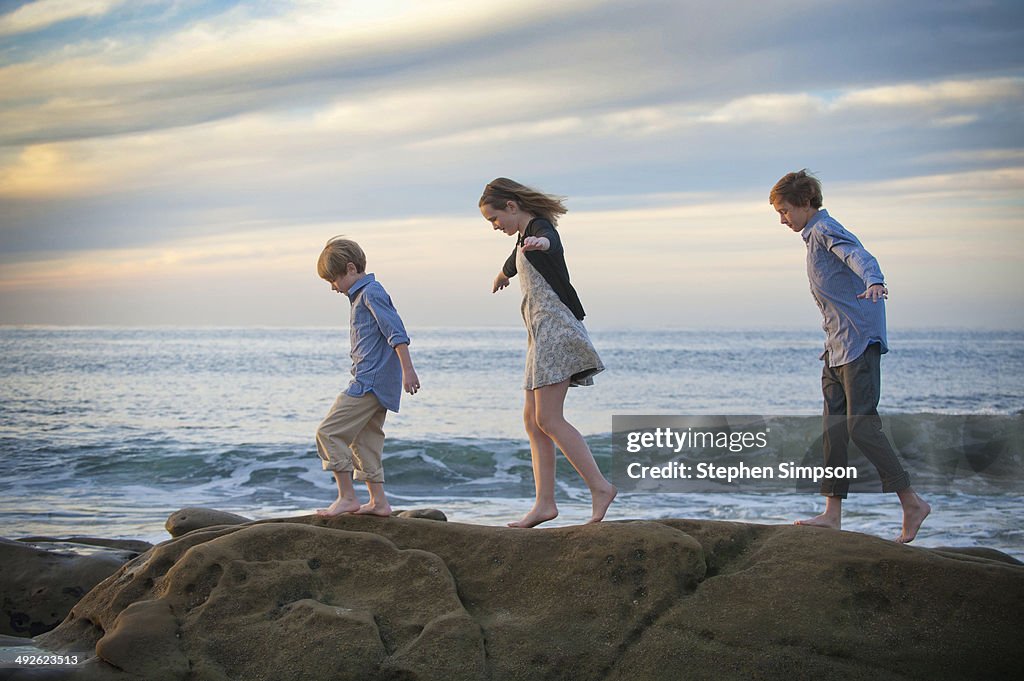 Siblings walking on seaside boulders