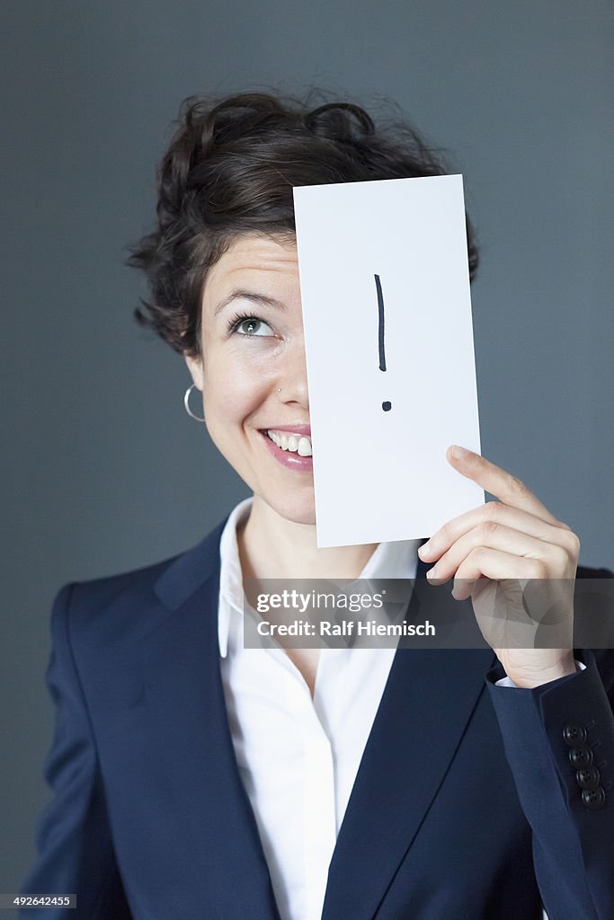 Mid adult woman holding paper with exclamation mark and smiling, close-up