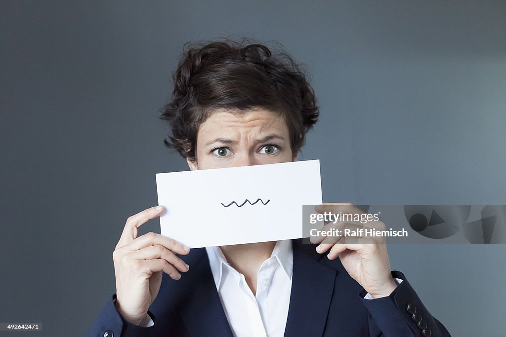 A worried looking woman holding paper with squiggle sign