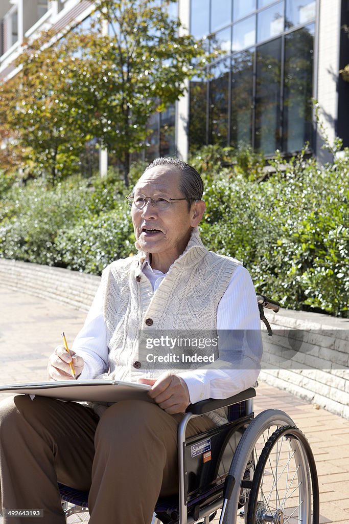 Senior man in wheelchair drawing on sketchbook