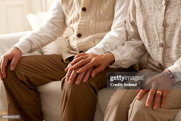 senior couple holding hands on sofa - hand on knee photos et images de collection