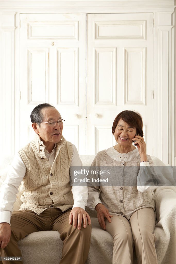 Senior woman talking on mobile phone next to her husband on sofa