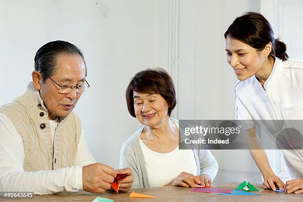 senior man making origami, senior woman and caregiver looking at him - folding origami stock pictures, royalty-free photos & images