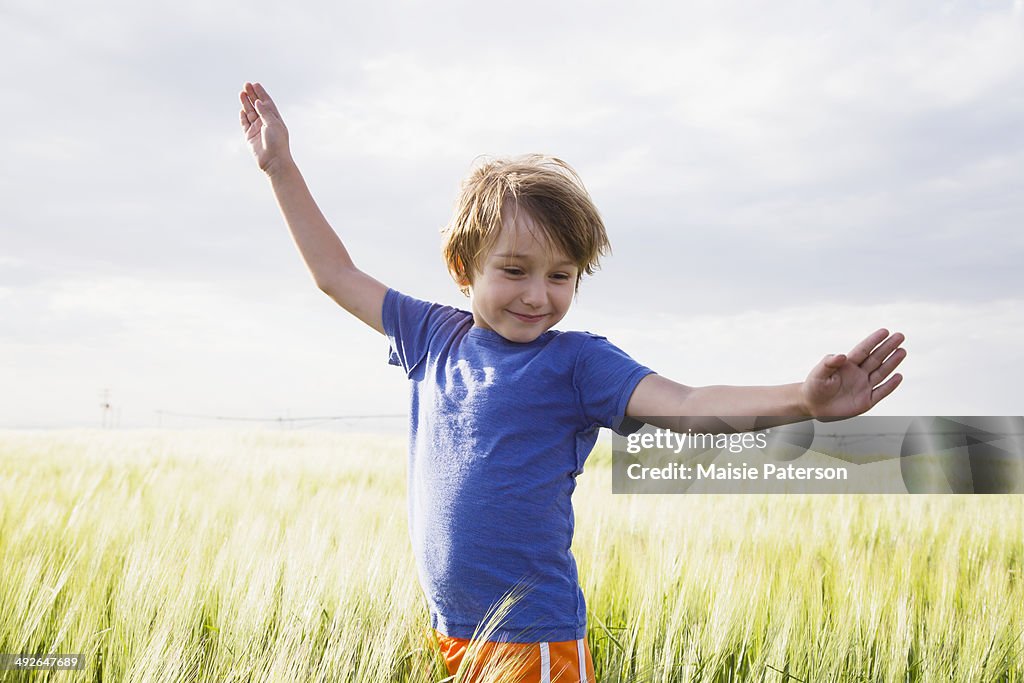 Boy (4-5) standing in grass with raised arms, Barley, Colorado, USA