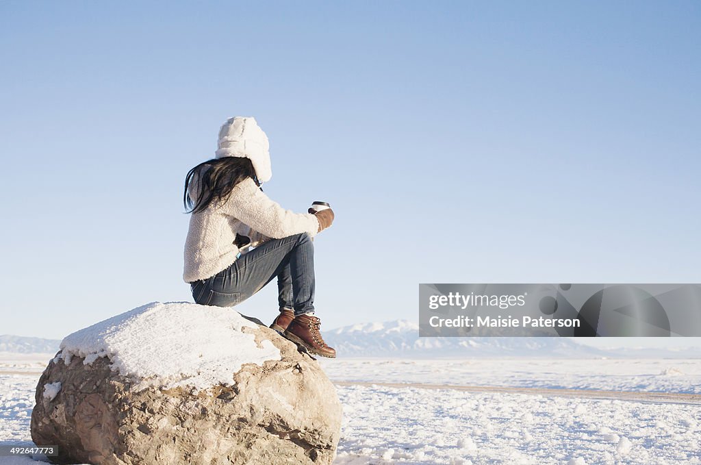 Woman sitting on rock with cup in winter, Colorado, USA