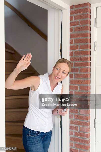 woman opening door and waving, goirle, brabant, netherlands - woman waving goodbye photos et images de collection