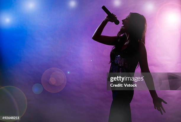 silhouette of female singer on stage - sängerin stock-fotos und bilder