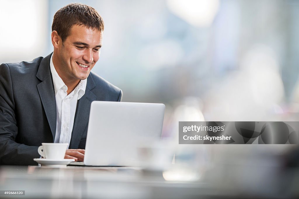 Smiling businessman using computer on a break in a cafe.