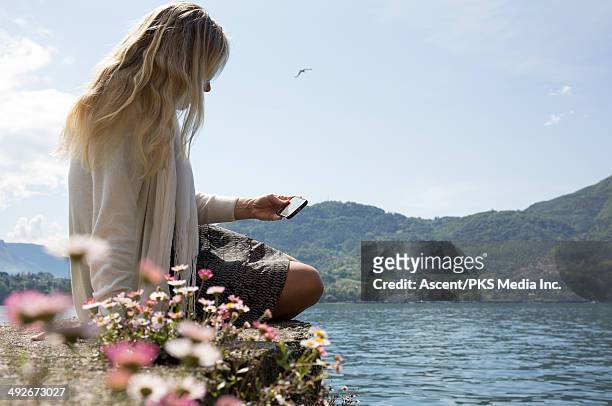 view past flowers to woman sending text above lake - lake como stock-fotos und bilder