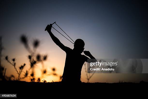 Palestinian protestor uses a sling shot to throw stones at Israeli soldiers near the border fence between Israel and the Gaza Strip after clashes...