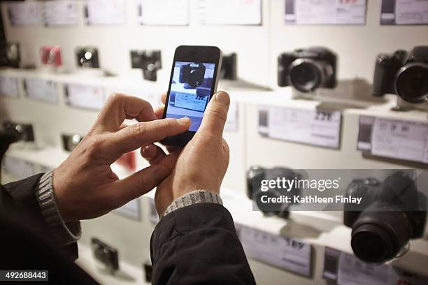 mid adult man photographing camera's in shop display using smartphone - digitalkamera bildschirm stock-fotos und bilder