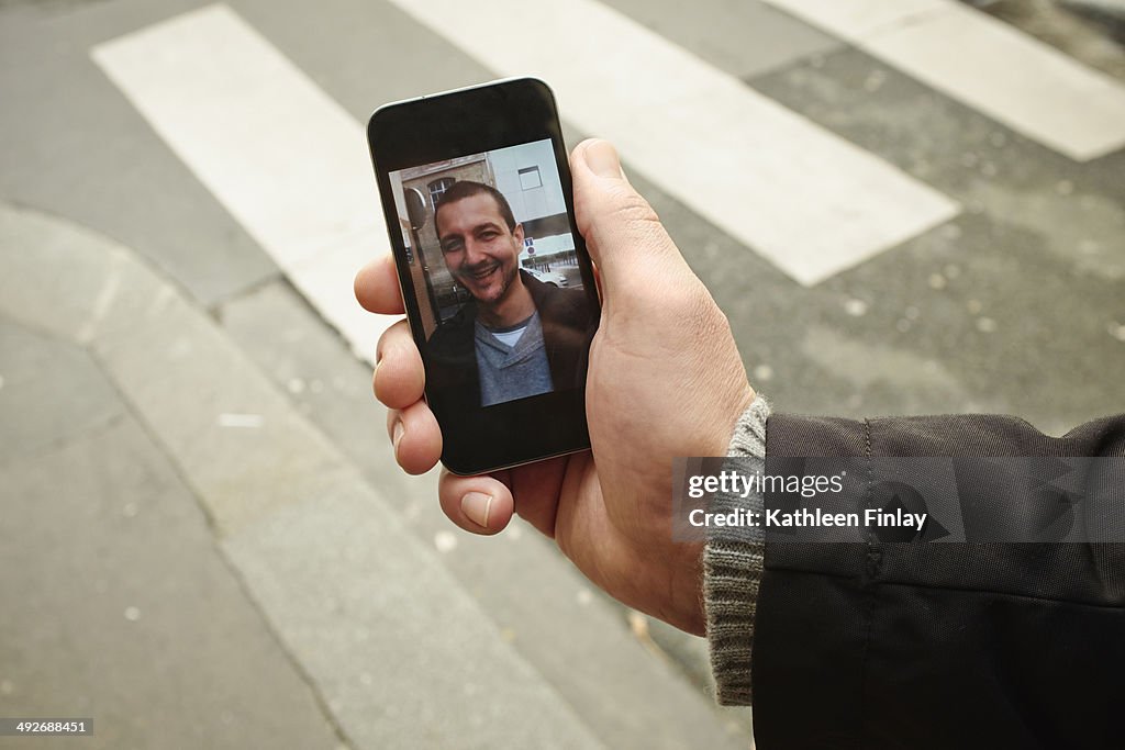 Mid adult man on sidewalk holding smartphone with photograph on screen