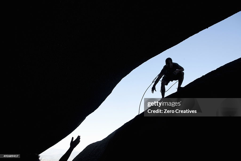 Silhouette of young male climbers reaching out for each other on rock