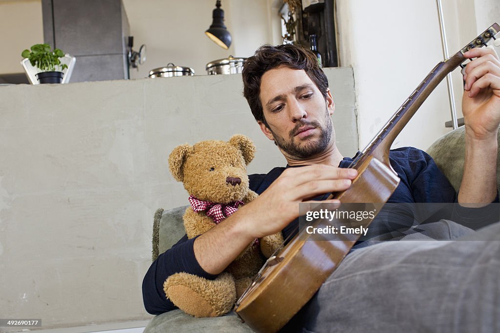 Mid adult man reclining on sofa playing guitar