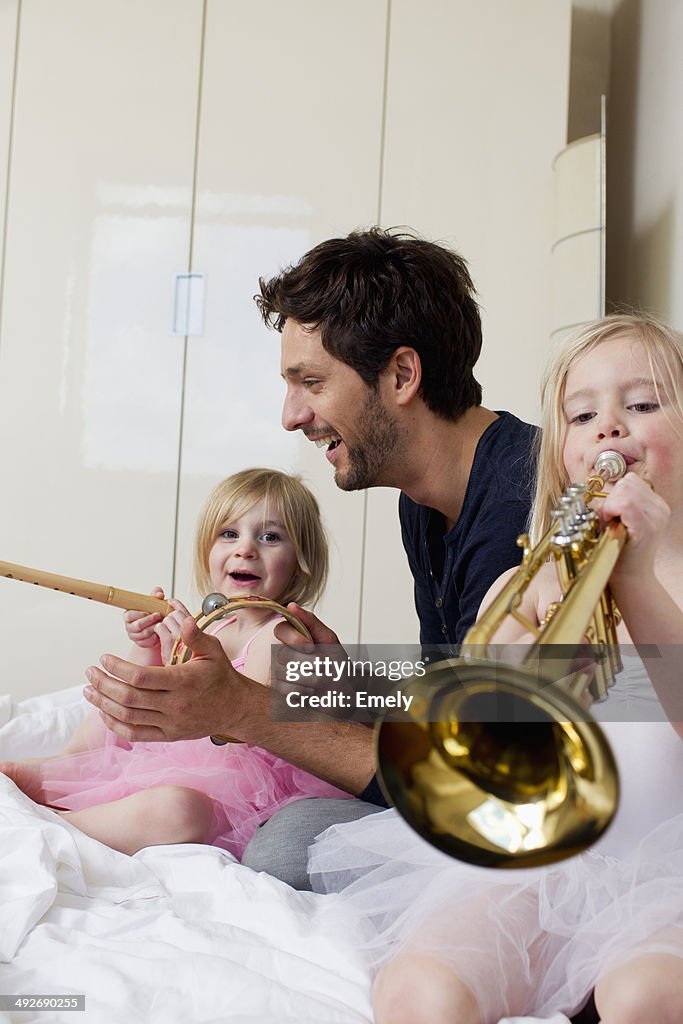 Father and two young daughters playing music