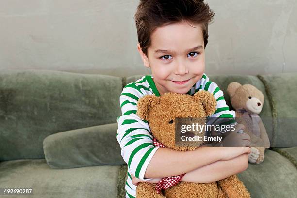 portrait of young boy on sofa hugging teddy - stuffed toy stock pictures, royalty-free photos & images