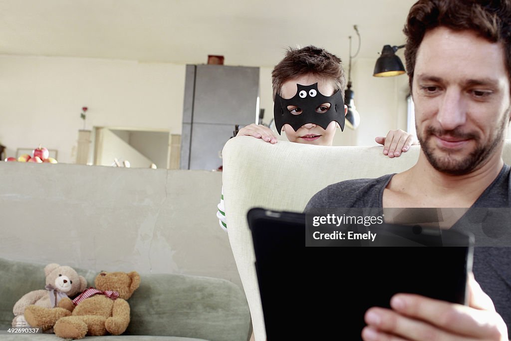 Masked son distracting father from digital tablet