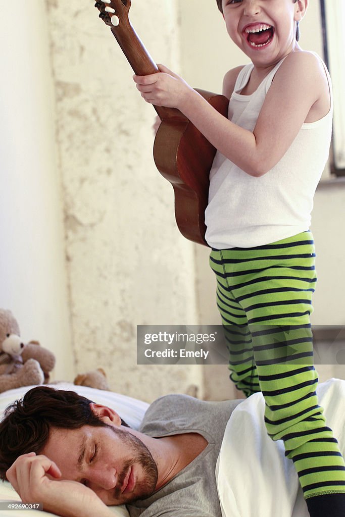 Son playing guitar whilst his father sleeps