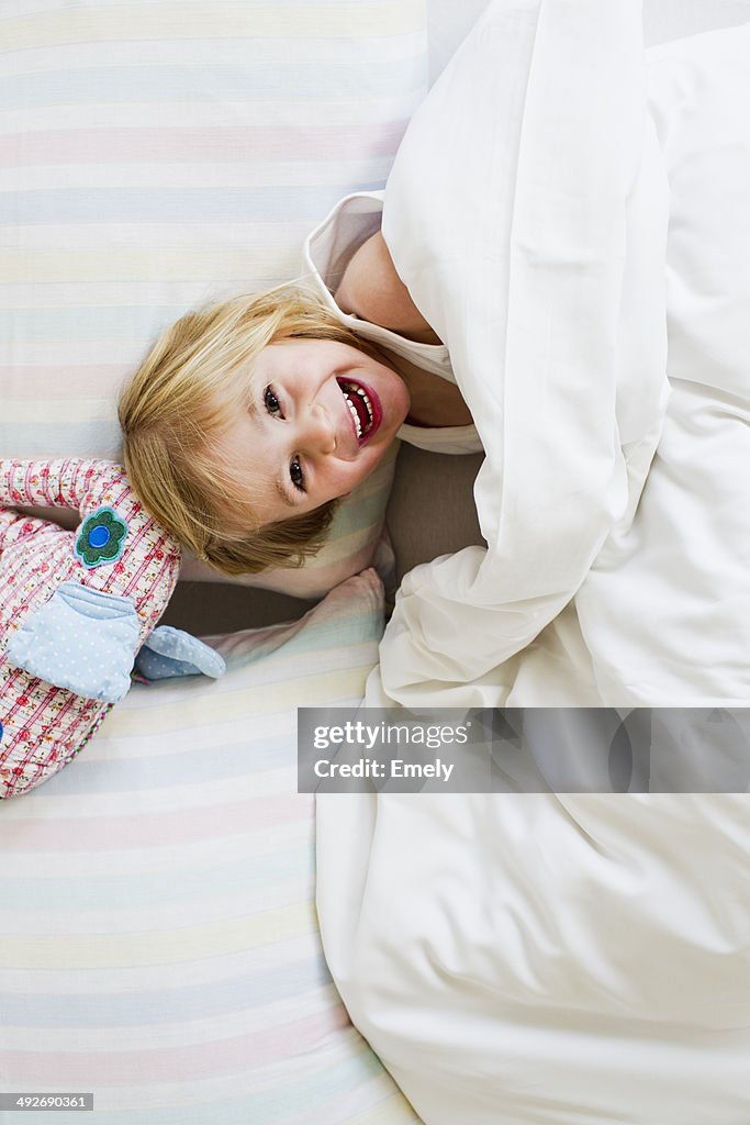 Portrait of young girl lying in bed with toy elephant