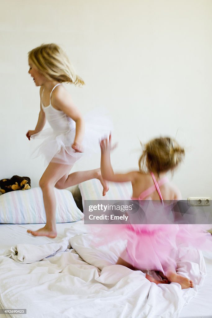 Sisters dressed as ballet dancers running on bed