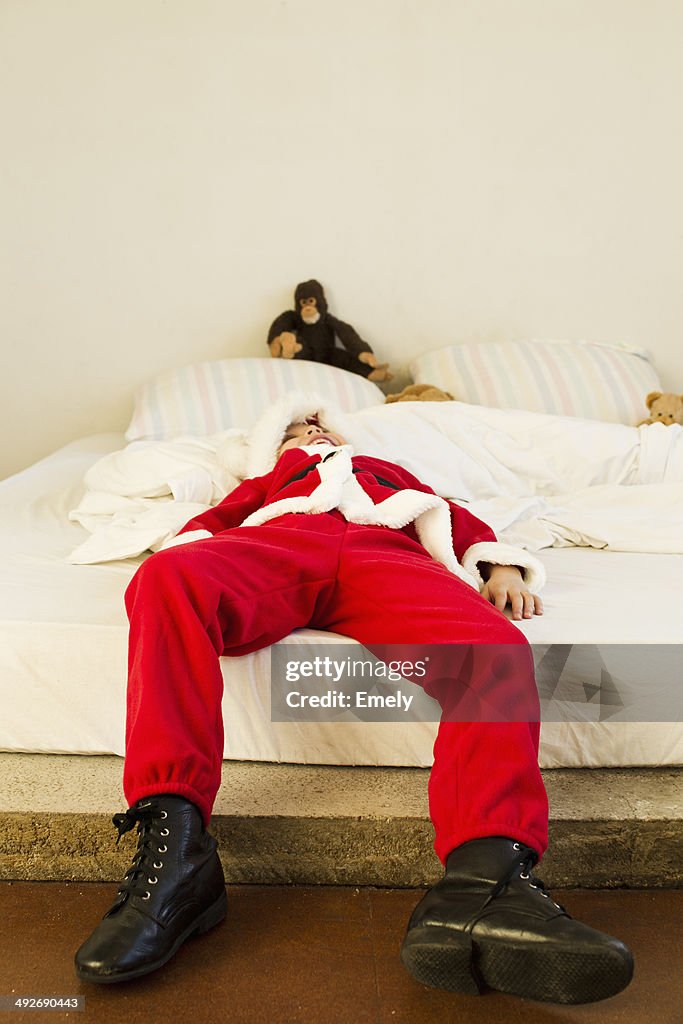 Young boy dressed up as santa claus lying on bed