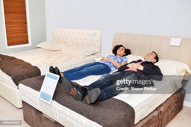 couple lying on bed in furniture shop showroom - materasso foto e immagini stock